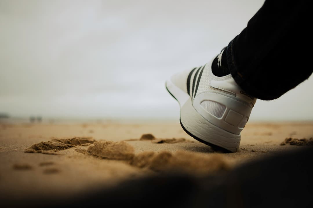 a foot wearing adidas trainers raised on top of a sandy beach